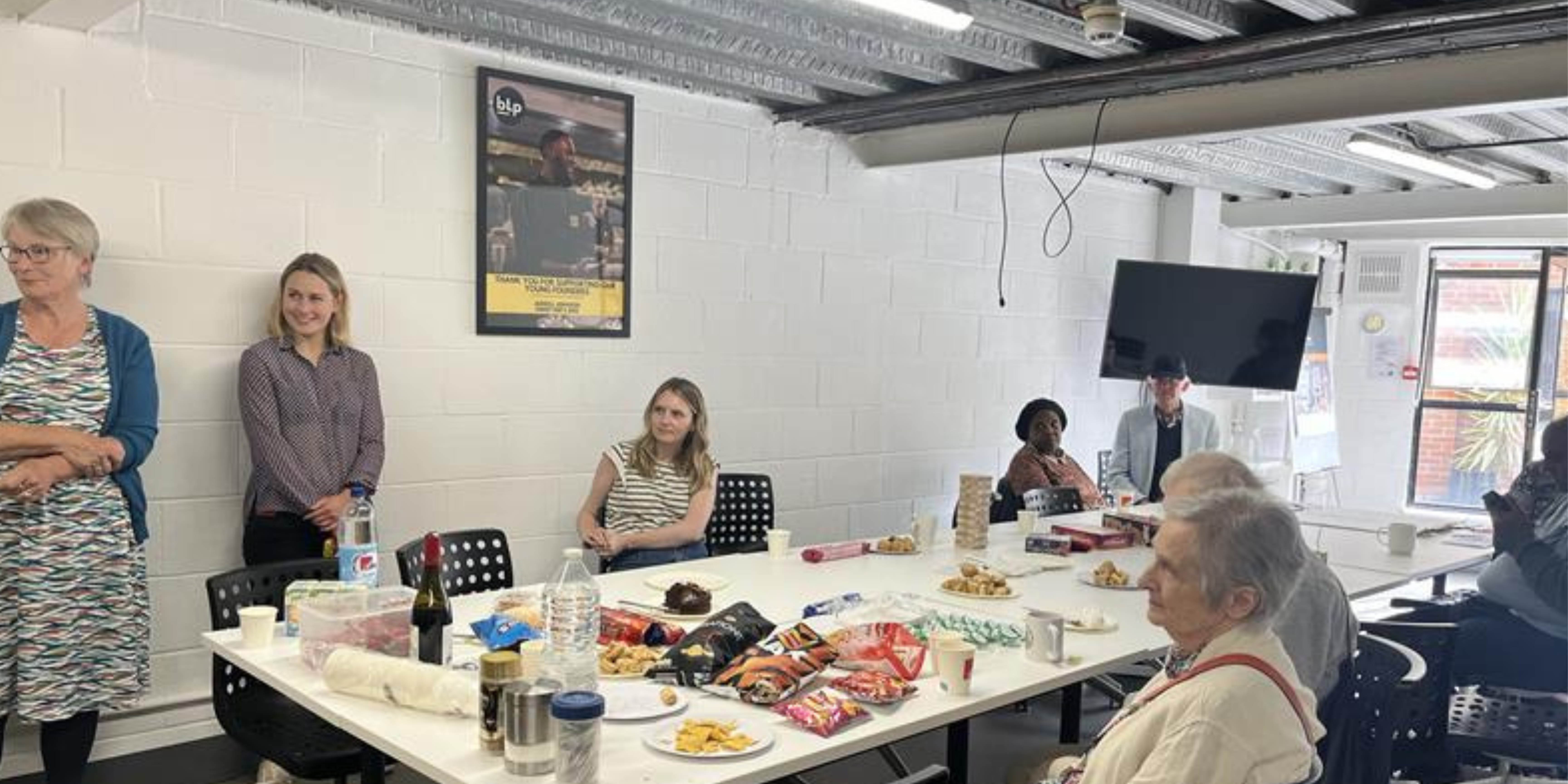 Healthwatch volunteers sitting around a table with food on it, conversating.