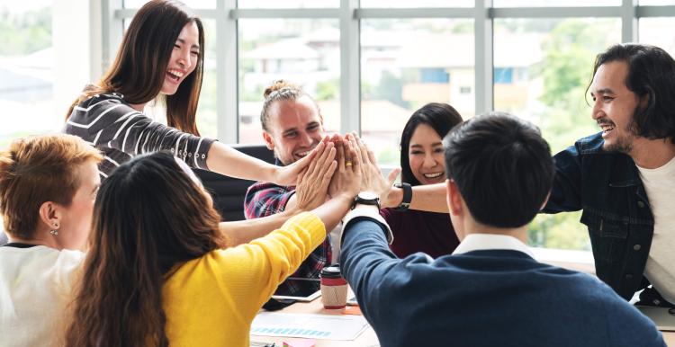 group of people around a table all putting their hands in the middle to high five each other