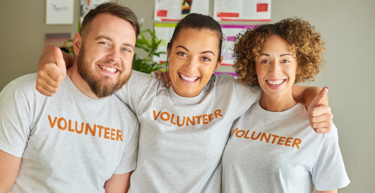 3 people smiling, looking at camera with volunteer written on their white top