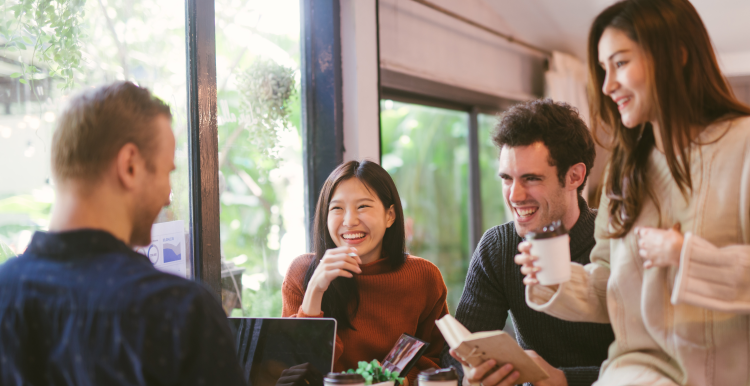 People gathered together on a table, with laptops and coffee, having a discussion.