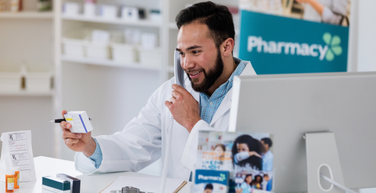 Pharmacist behind the counter, on the phone and holding a medicine box looking at it and smiling
