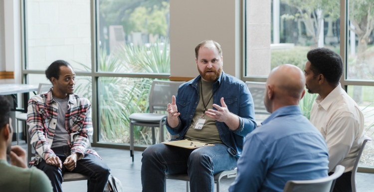 Men sitting on chairs around a circle in a group setting, having a discussion