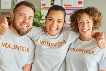 3 people smiling, looking at camera with volunteer written on their white top