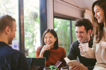 People gathered together on a table, with laptops and coffee, having a discussion.