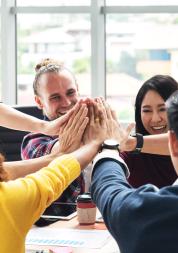 group of people around a table all putting their hands in the middle to high five each other